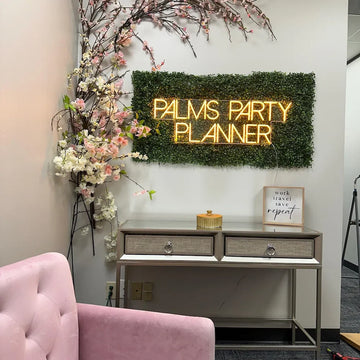 Enseigne néon jaune « Palms Party Planner » sur un mur végétalisé dans un intérieur